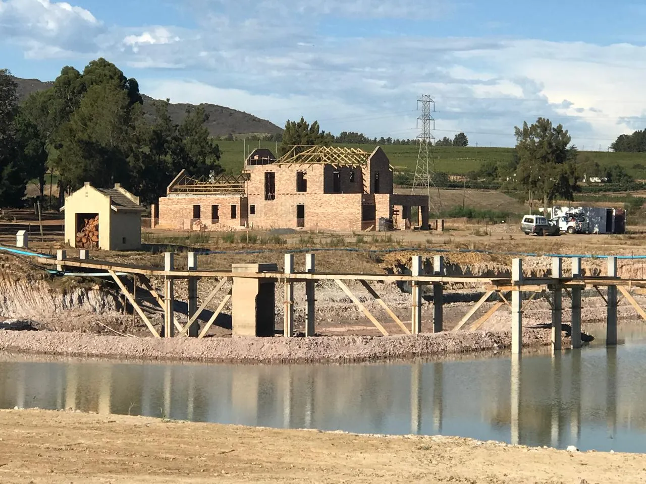Two-storey Devonvale residence with its roof trusses up, seen across the estate dam and vineyards